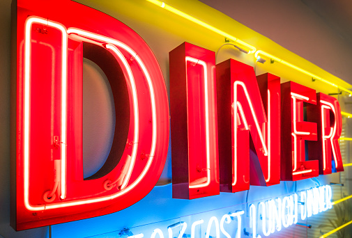 Close-up of a large old fashioned diner sign, glowing in red, blue and yellow.