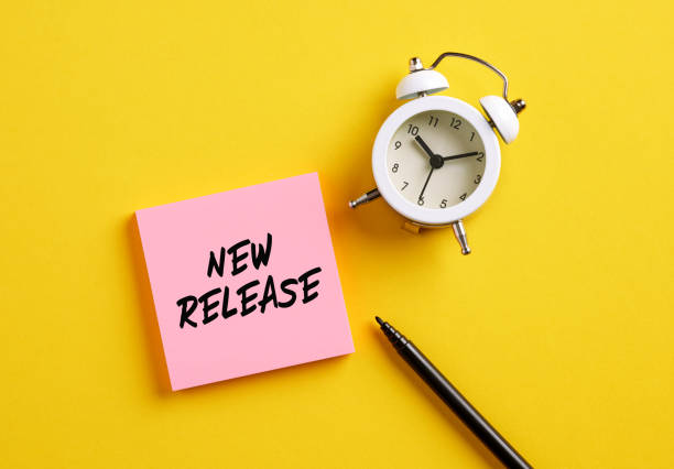 New release message on pink note paper with alarm clock and pen. Marketing concept for new publishing and advertising products. New release message on pink note paper with alarm clock and pen. Marketing concept for new publishing and advertising products. release notes stock pictures, royalty-free photos & images