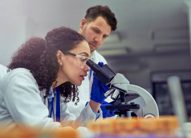 istock Side view of female scientist looking at test sample through microscope in laboratory 1530246176