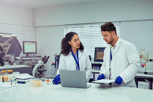 Female scientist talking to male colleague and discussing work with laptop in laboratory