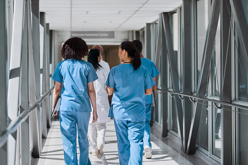 Female nurses walking with team of doctors and coworkers in hospital corridor
