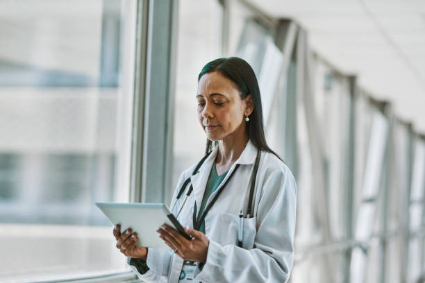 istock Female doctor looking at digital tablet beside window in corridor 1530248120