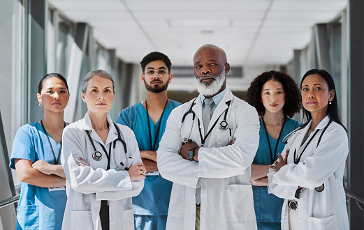 Team of senior doctors and nurses crossing arms and looking at camera in corridor