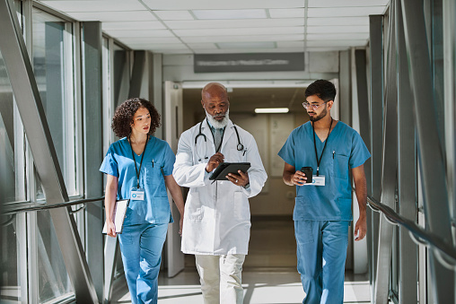 Senior doctor looking down at digital tablet, walking together with nurses in hospital corridor