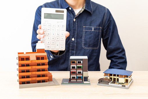 Man holding a calculator in front of a house model