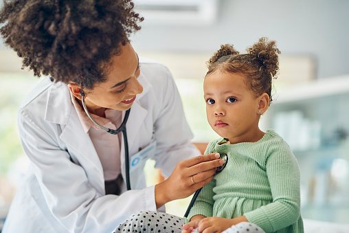 Little girl sitting still and looking into distance, patiently allowing female doctor listening to her chest with stethoscope in clinic