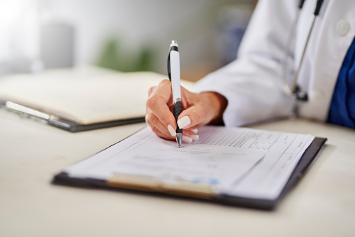 Female doctor with painted nails writing report on clipboard