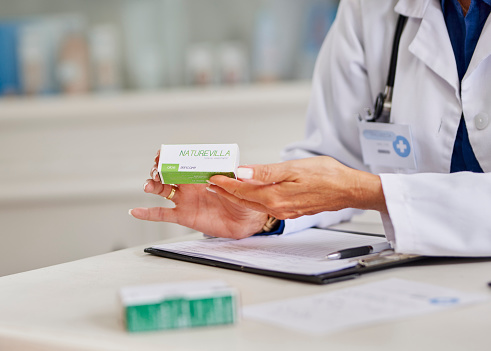 Doctor holding box of medication over clipboard at clinic desk