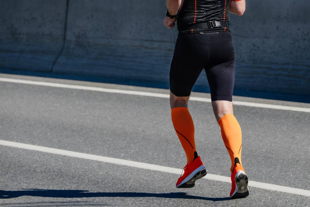 vue latérale athlète masculin en chaussettes de compression course marathon course sur route, événement sportif d’été - running marathon jogging track event photos et images de collection