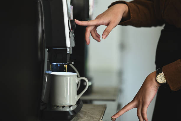 vista laterale della donna che prepara il caffè aromatico fresco, utilizzando una macchina da caffè nell'accogliente cucina dell'ufficio. - pouring coffee human hand cup foto e immagini stock