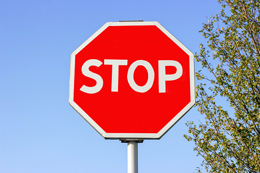 Bright red and white Stop traffic sign against the blue sky.