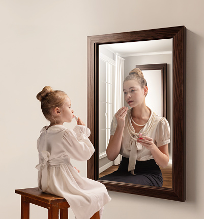 Creative conceptual collage. Little girl looking in mirror and seeing reflection of young girl, her future self. Aging. Concept of present, past and future, age, lifestyle, memories, generation, ad