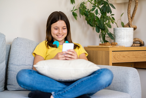 Smiling girl whit headphones using mobile phone on sofa at home