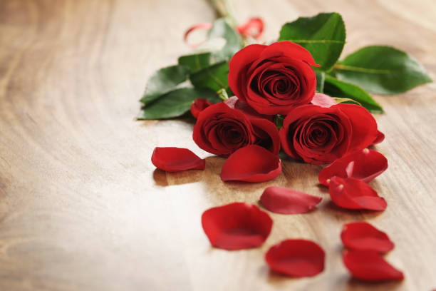 istock three red roses and petals on old wood table with copy space 1530334361