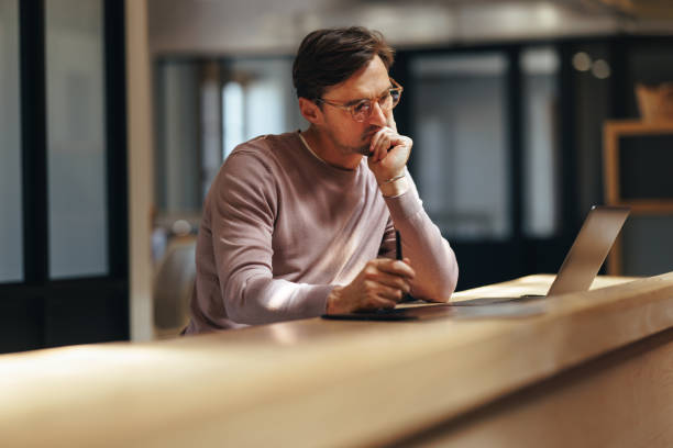 Thoughtful web designer working with a laptop in a coworking office Pensive web designer working on a project in a coworking office. Male designer thinking and looking at his design on a laptop. Creative business man working with a graphic tablet. mid adult men stock pictures, royalty-free photos & images