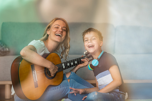 Happy woman playing guitar and singing whit her son at home