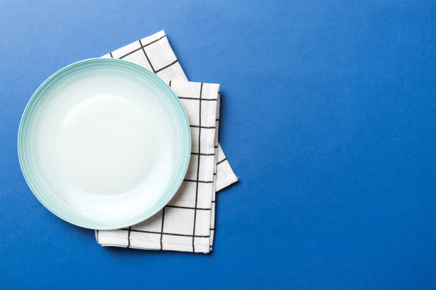色の背景に上面図、食品用のテーブルクロスに空の丸い青のプレート。あなたのデザインのためのスペースを持つナプキンの空の皿