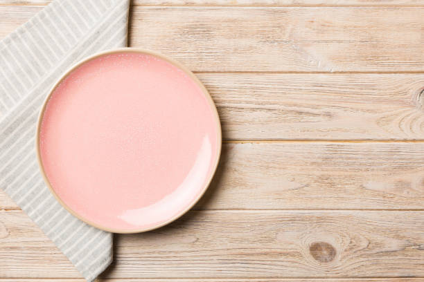 色の背景に上面図、食べ物用のテーブルクロスに空の丸いピンクのプレート。あなたのデザインのためのスペースを持つナプキンの空の皿