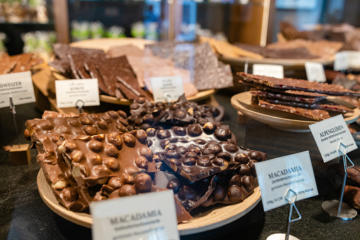 A close up of a shop window of a chocolate factory in Garmisch in Southern Germany. They create and produce varied versions of some beautifully presented chocolates and sweet treats. In the window is multiple variations of toppings and flavours.