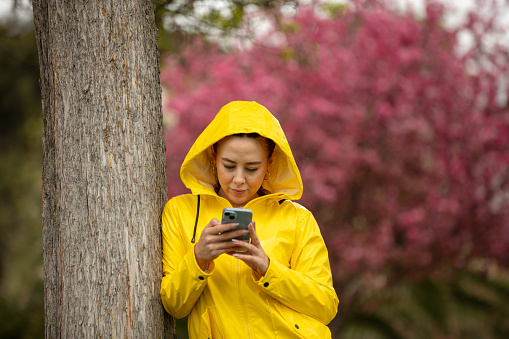 Young woman is typing a message on the outside in rainy day.