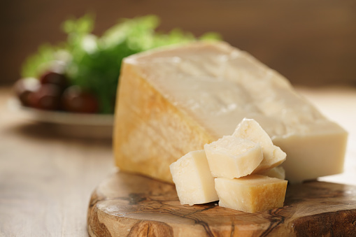 hard parmesan cheese cubes on olive cutting board, closeup photo