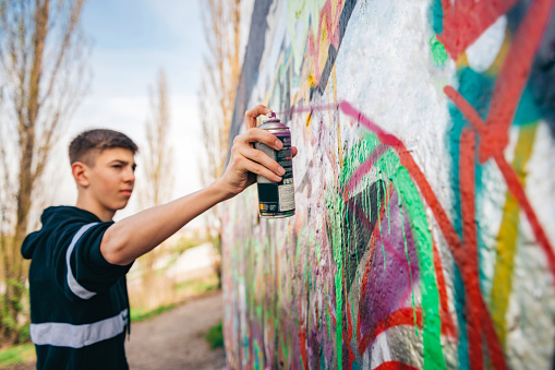 Street artist working on colored graffiti at public space wall - Modern art perform concept of urban guy painting live murales with yellow and orange aerosol color spray - Bright sunflare filter