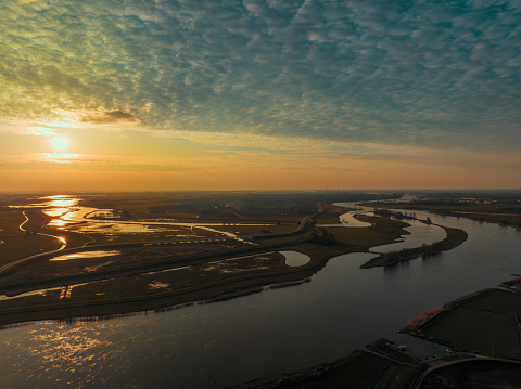 Panoramic aerial view on the river IJssel and Reevediep Bypass waterway during a springtime sunset in Overijssel. The flow of the river is leading towards the setting sun in the distance while lights are popping up in the city at the end of a beautiful springtime day.