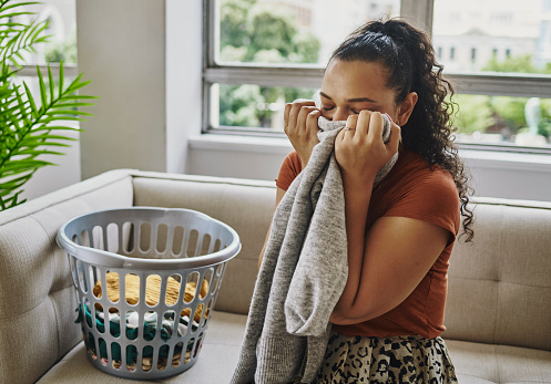 A young woman sitting and smelling her fresh and clean laundry at home. Stock photo, copy space