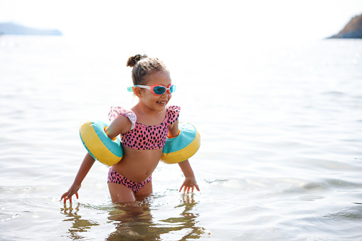 Child learning to swim in outdoor sea of tropical resort. Kids learn swimming. Exercise and training for young children. Little boy with colorful float board in sport club. Swimming baby or toddler.