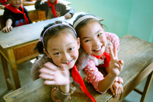 Two Chinese elementary school students are shaking hand and posing victory sign to camera.