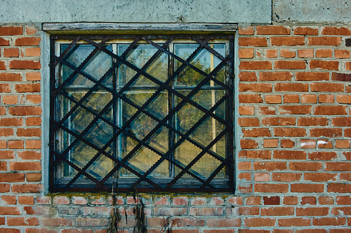 An old brick building, a window with wooden frames, a grate on the window made from pieces of a band saw, interesting places in the city