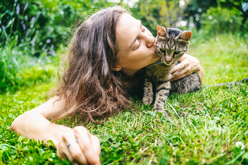 Portrait of happy young woman kissing cat lying on grass in summer garden