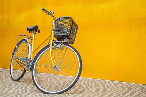 A yellow retro bicycle parking against yellow wall background.