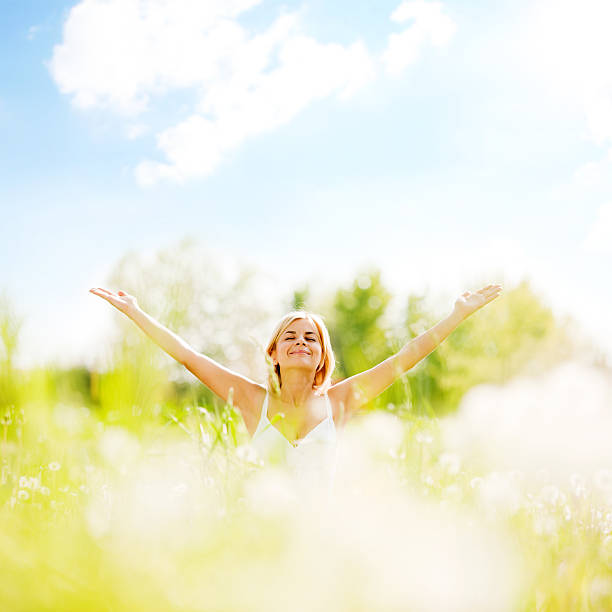 Pretty woman with her eyes closed is sitting in the nature with her arms spread widely.  