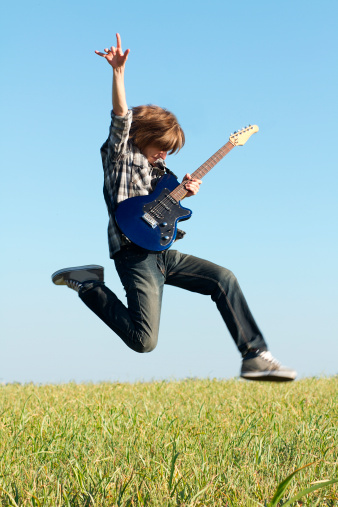 Young rocker posing with musical instrument outdoors at bright summer day