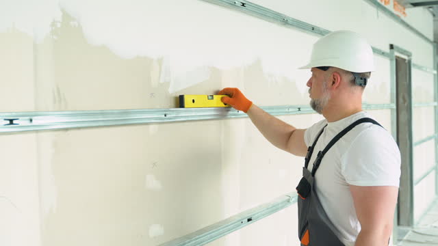 A man builder measures of the horizontal deviation of plasterboard wall