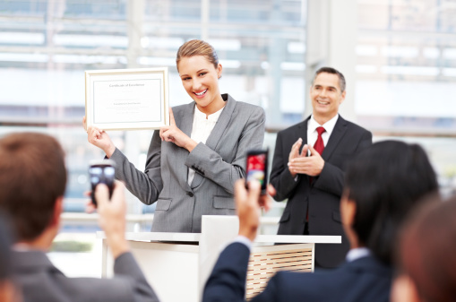 Attractive businesswoman receives applause on stage while holding up an award. Horizontal shot.