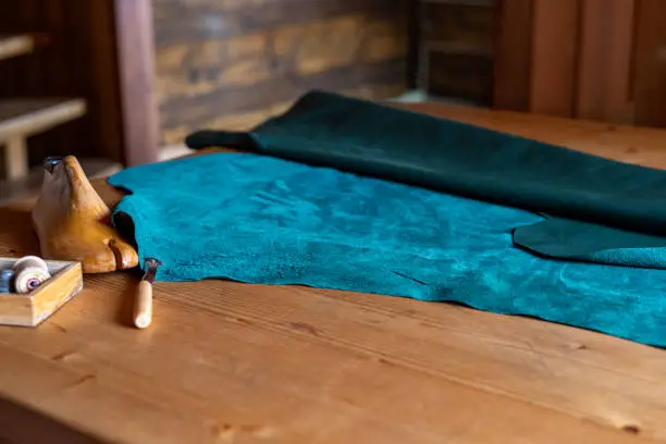 Blue-green genuine leather for sewing shoes and clothes on the table. shoemaker's workshop