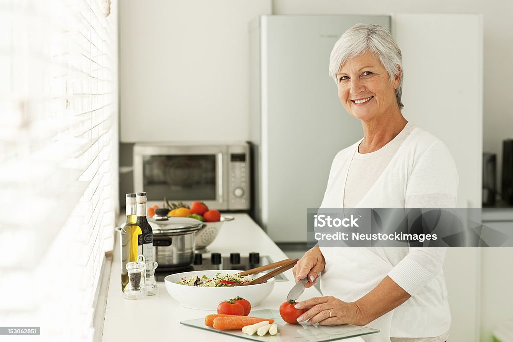 Улыбается Старший женщина резки овощей в кухне - Стоковые фото 60-64 года роялти-фри