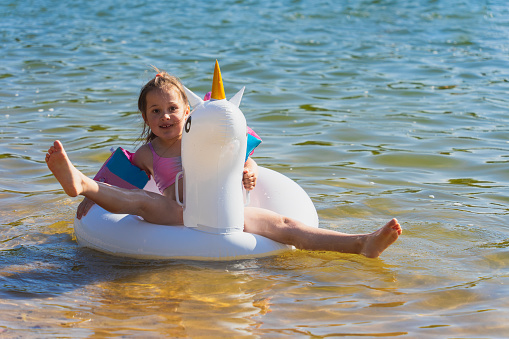 A little girl swims in the sea on an inflatable unicorn ring on a summer day. High quality photo
