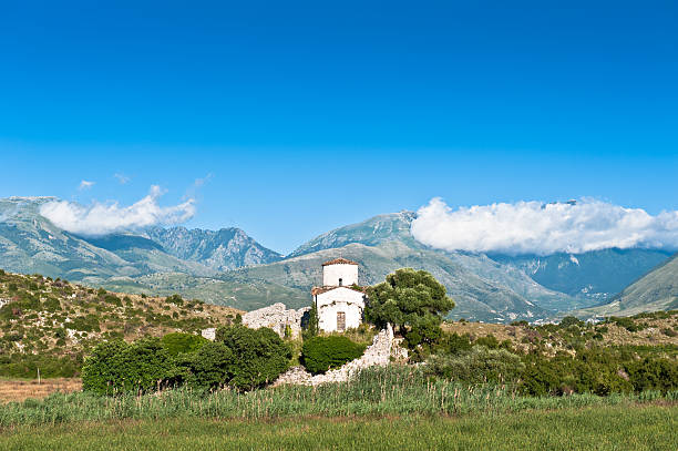 Small stone church with a shiny copper dome on a hill surrounded by trees and graves. Scenic mountain landscape with lake in the background. Religious building in peaceful natural setting.