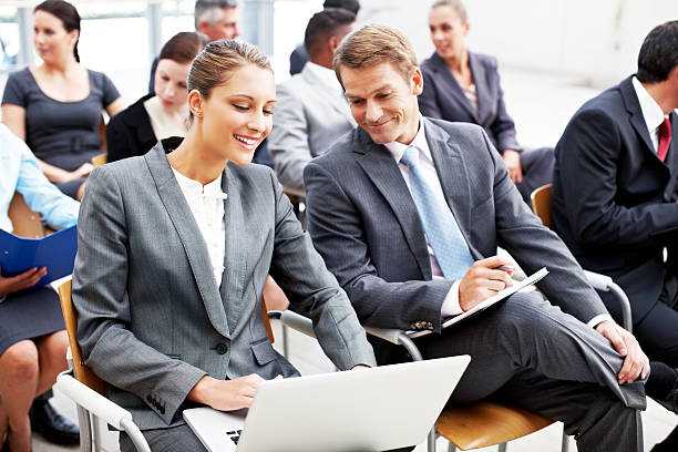 Businessman and businesswoman work together on a laptop while sitting at a conference. Horizontal shot.