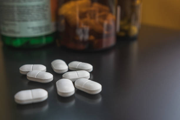 istock White pills on a black surface, selective focus, close up. Defocused medicine bottles in the background. 1530660819
