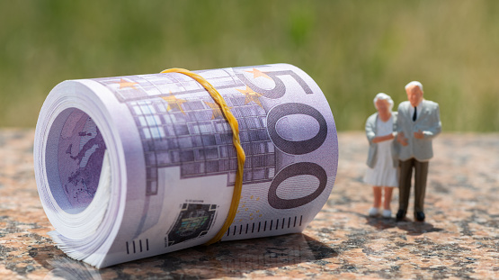 A stack of banknotes in denominations of 500 euros and figurines of an elderly couple