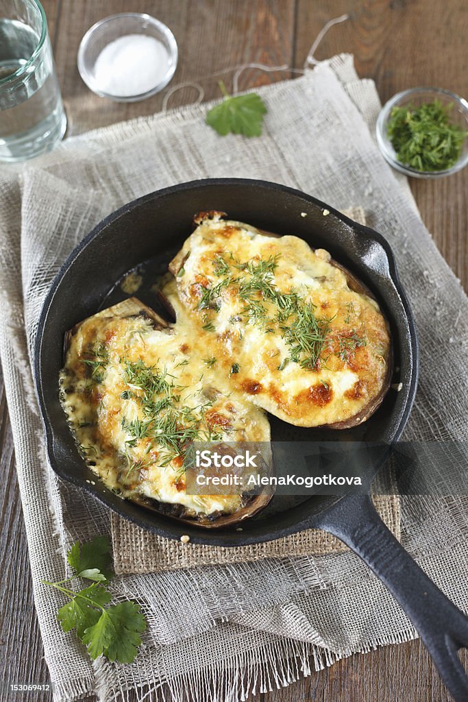 Stuffed Eggplants with Cheese Stuffed Eggplants with minced meat and cheese in a cast-iron pan which is on a pile of linen cloths. Baked Stock Photo
