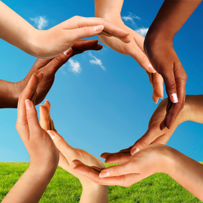 Conceptual peace and cultural diversity symbol of multiracial hands making a circle together on blue sky and green grass background.
