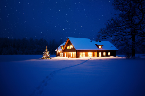 Illuminated house with christmas tree beside it in wintery scene with footpath to it.