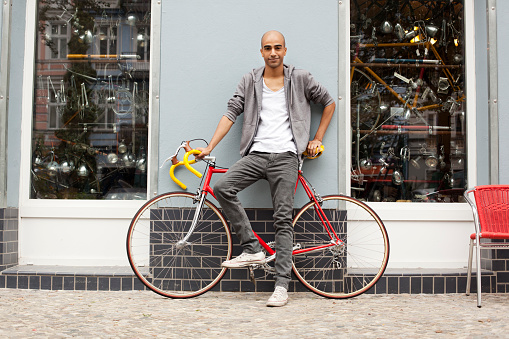 Young cool guy with a racing bike in the streets of berlin in front of a bike shop.