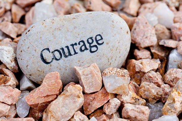 Courage written on a big smooth rock with jagged rocks close up of 'courage' stone on textured stone background courage stock pictures, royalty-free photos & images