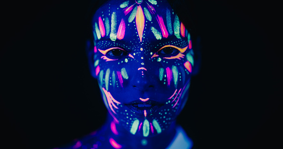 Innovative Beauty Advertising Shoot: Talented Model Showcases Her Unique Style, Neon-Painted Body and Face Contrasting Beautifully with Dark Backdrop, Creating a Visually Stunning Close Up Portrait